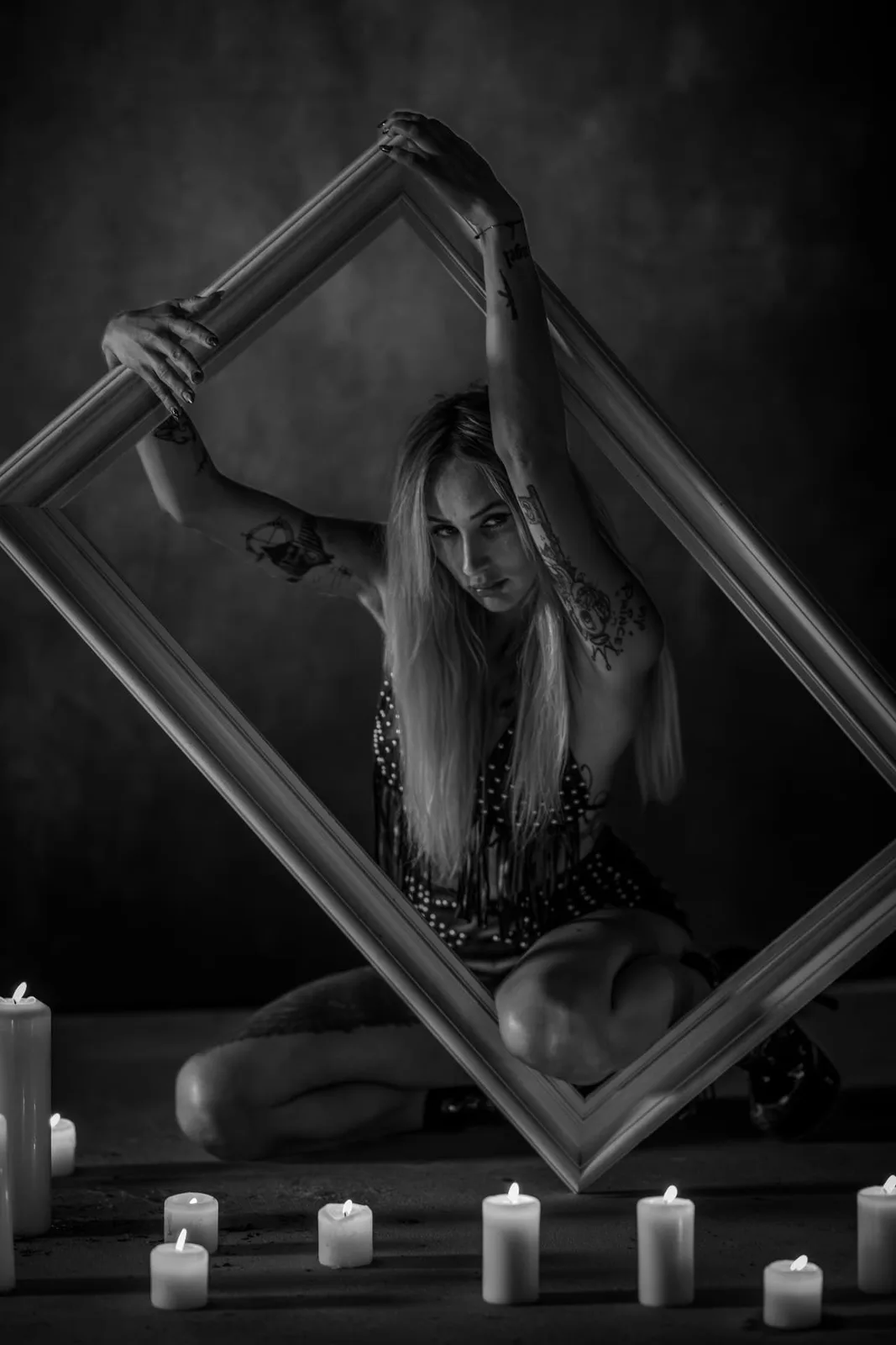 Black-and-white portrait of a woman with an empty picture frame and candles