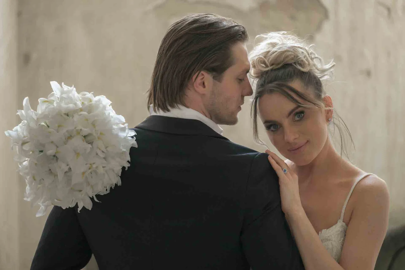 Editorial wedding portrait at Schloss Haggenberg — bride with a white bouquet leaning on the groom's shoulder, quiet fine-art wedding photography Austria