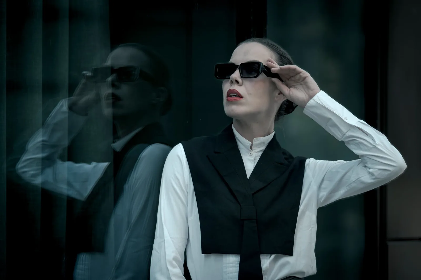 Model Denisa Strakova in front of dark glass facades around Messe Wien, her reflection doubling the frame in available light.