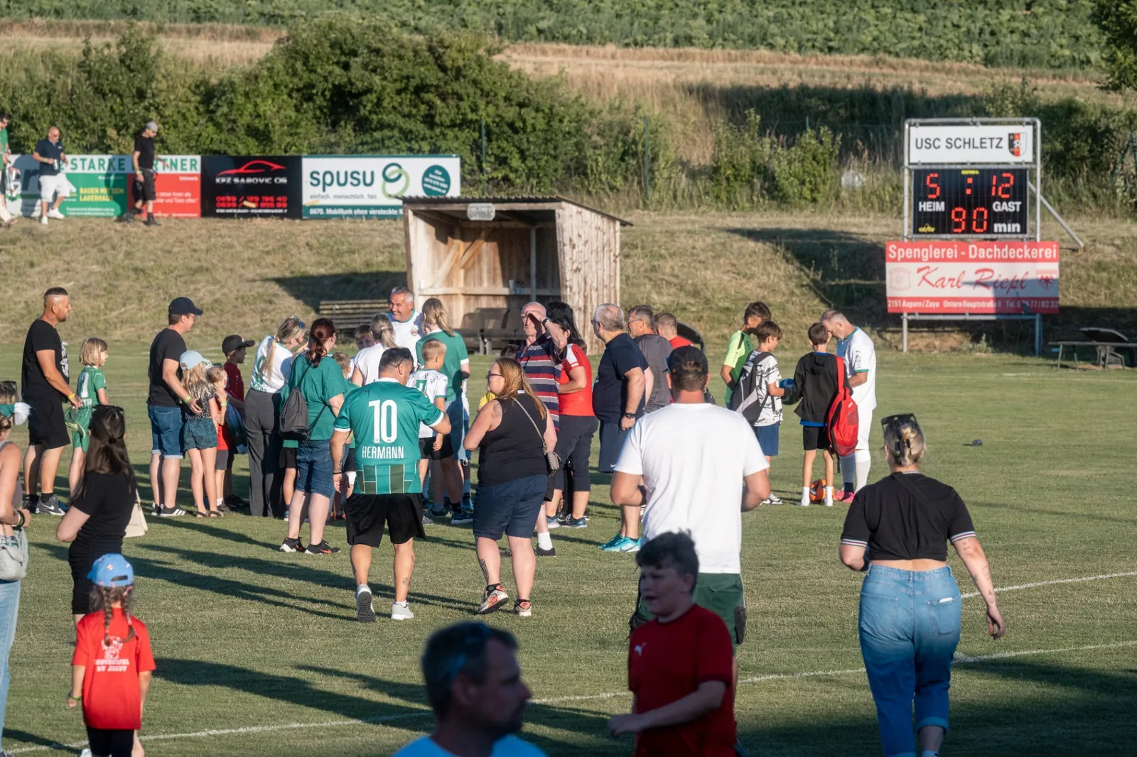 Zuschauer und Spieler auf dem Rasen des USC Schletz nach dem Schlusspfiff im warmen Abendlicht des Weinviertels.