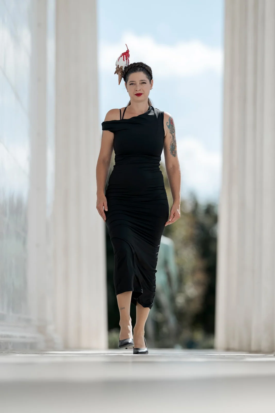 Full-length photograph of Asquina in a long black dress between the white columns of the Theseus Temple in Vienna