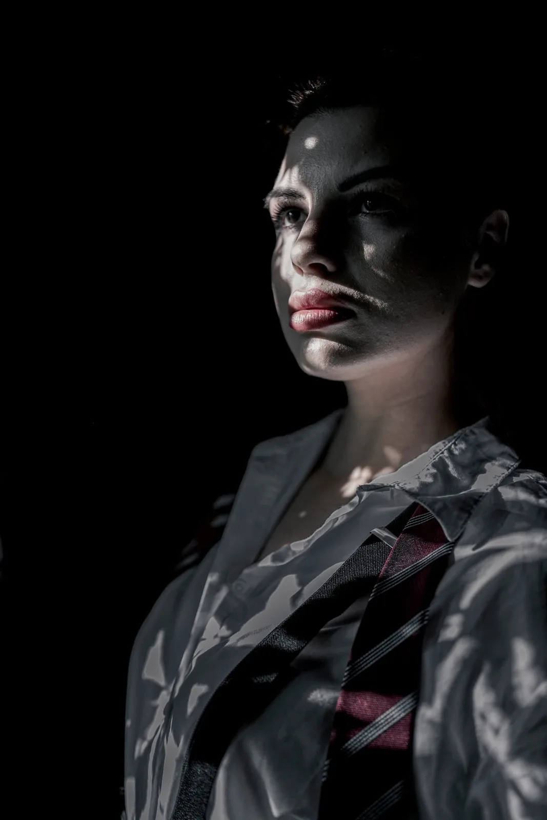 Editorial portrait of a woman in a white shirt and tie illuminated by structured light