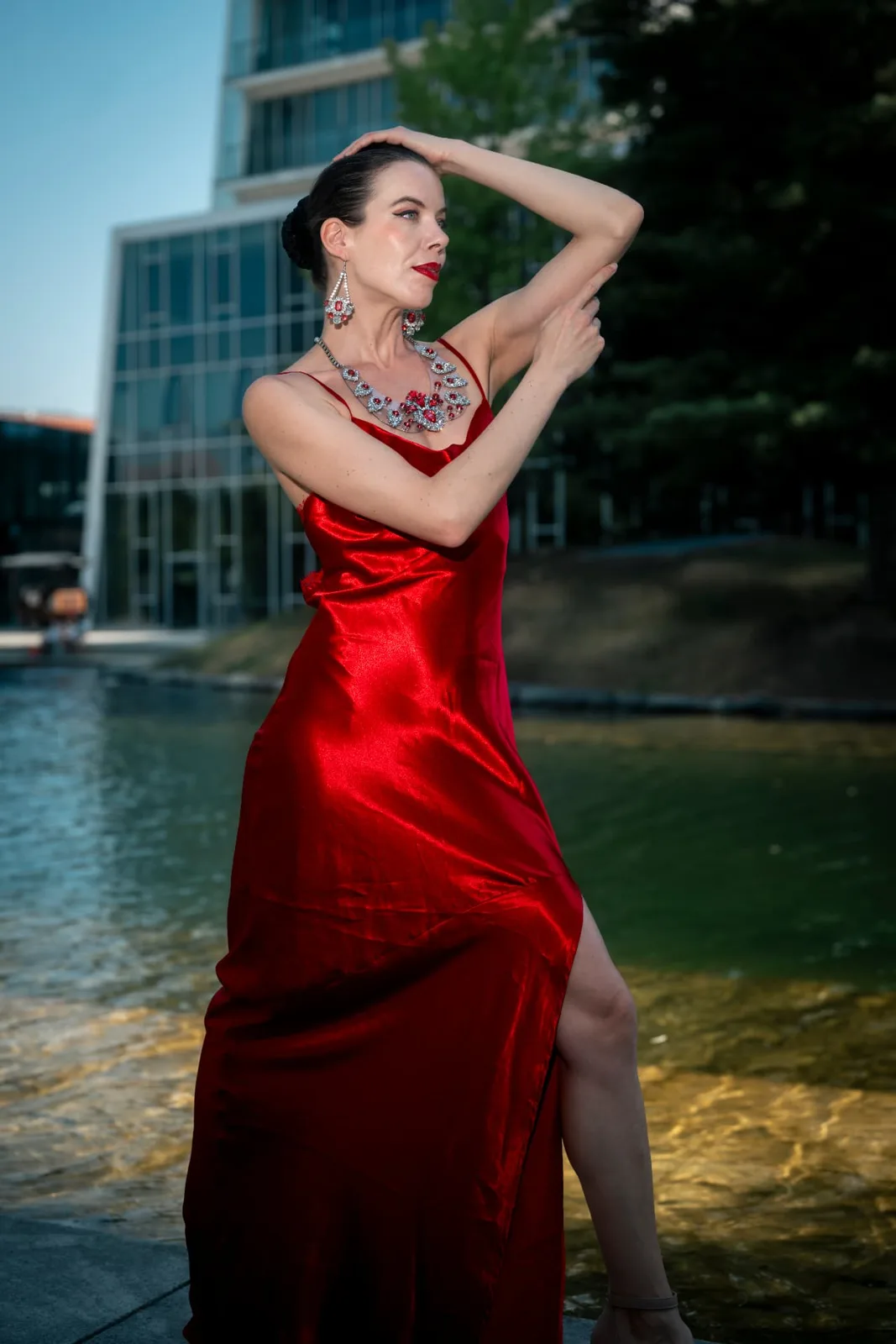 Model Denisa Strakova in a red gown posing beside the water basin at Messe Wien, contrast and colour controlled with off-camera flash.