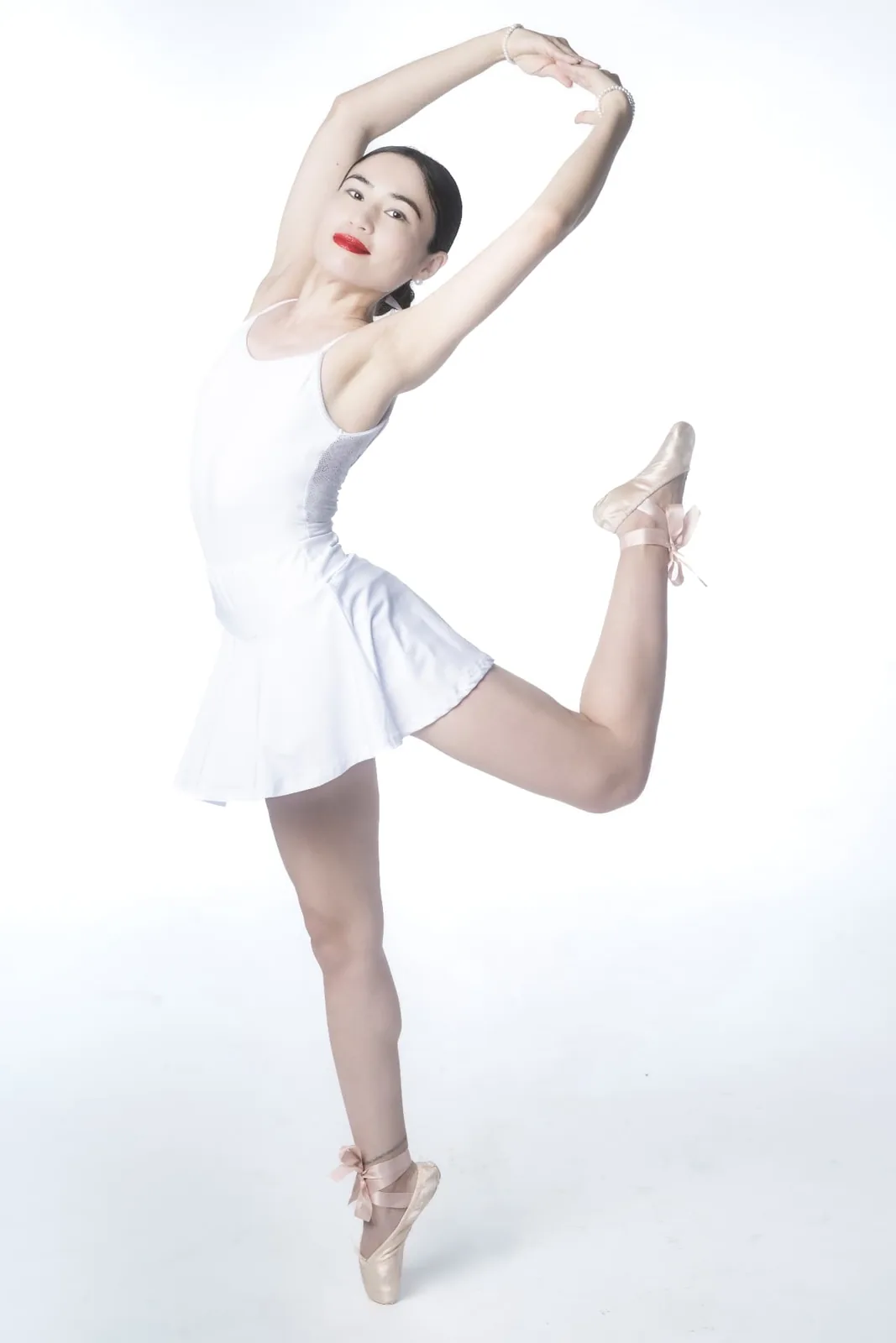 Attitude position photographed from the front, dancer Mia balancing en pointe in a white leotard and skirt.