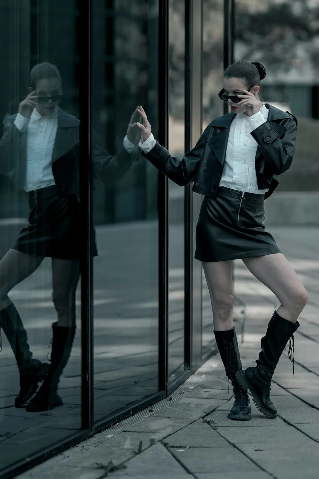 Denisa Strakova leaning against a glass facade near Messe Wien, her reflection mirroring the gesture.