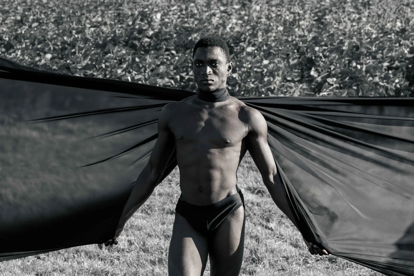 Monochrome editorial of Kevin holding black fabric wide open in a field in Lower Austria.