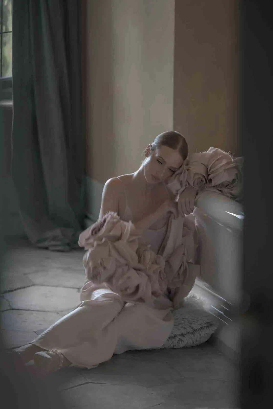 Editorial wedding portrait of the bride resting on the floor of a sunlit room during the final preparations.