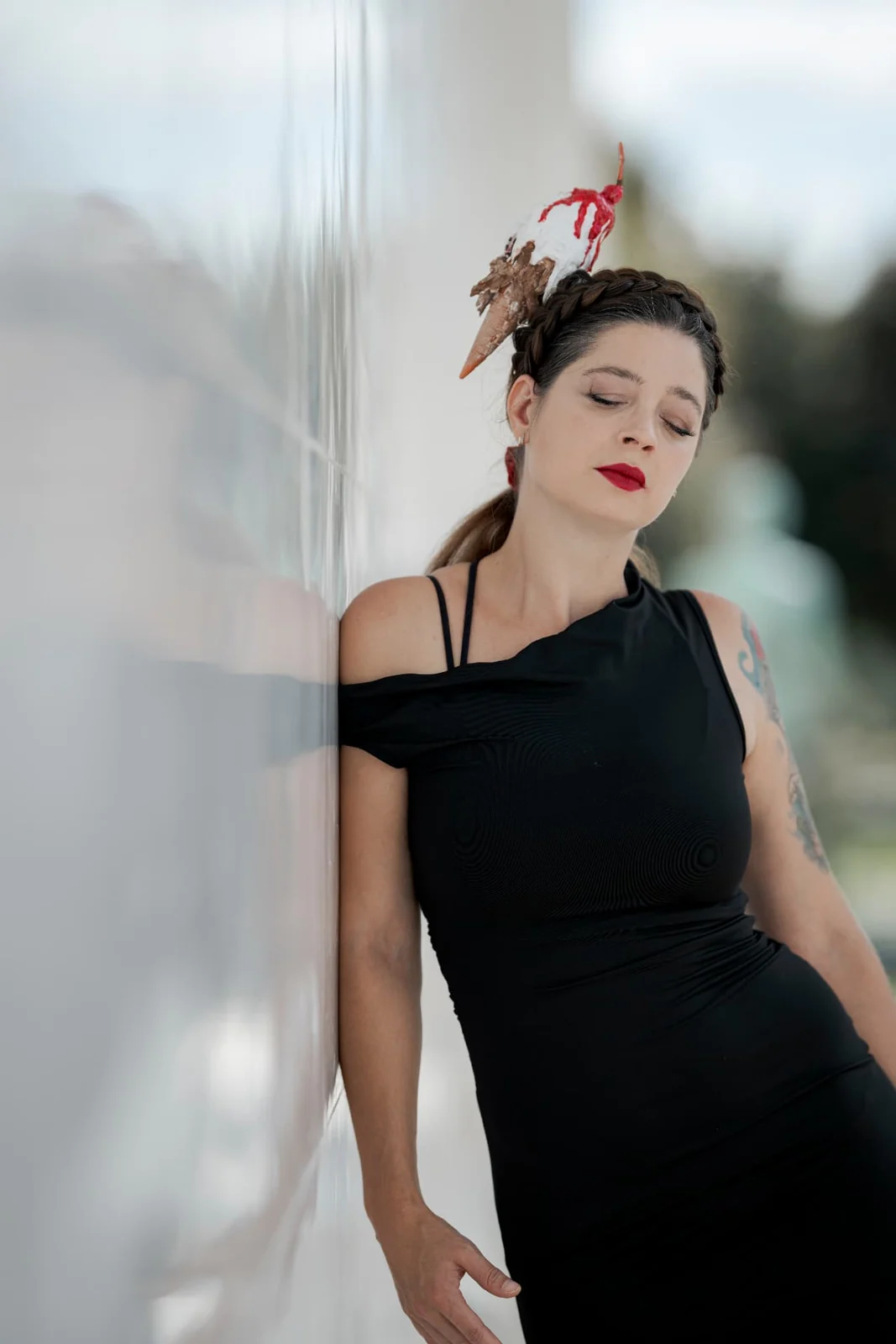 Half-length fashion portrait of Asquina in a black dress with a red accent against soft architecture
