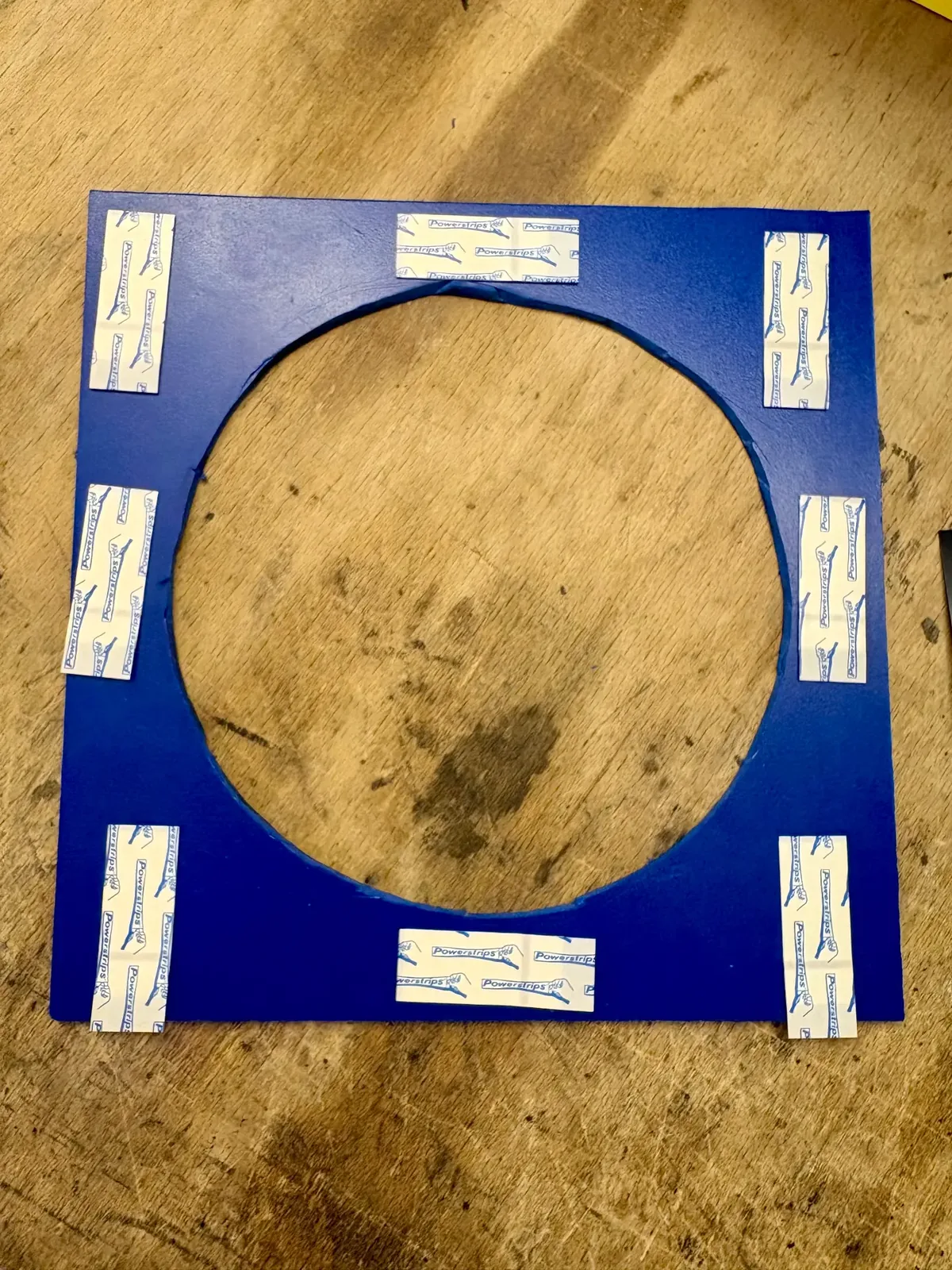Ausgeschnittener PVC-Rahmen mit vorbereiteten Tesa Powerstrips für die Montage.