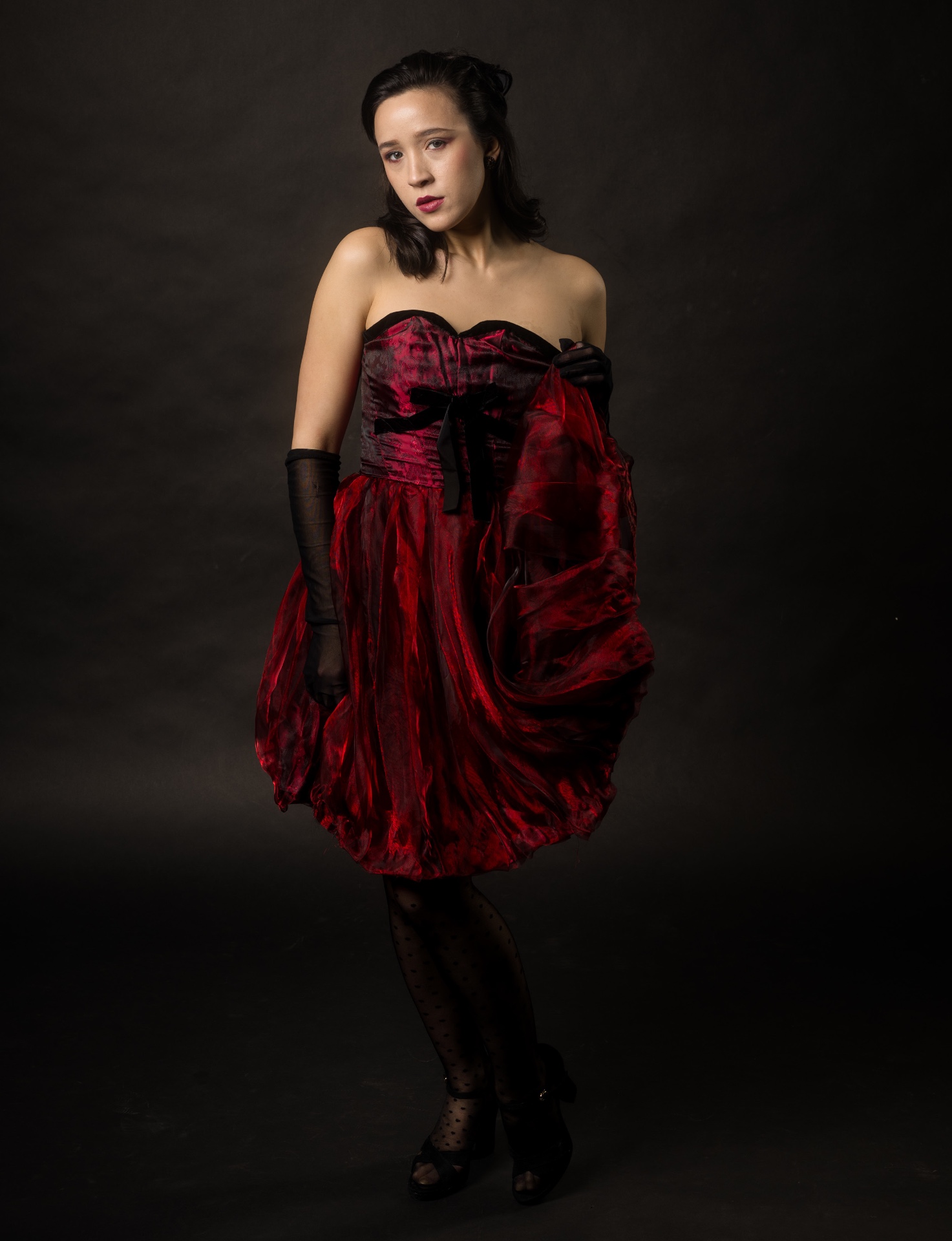 Crimson Poise editorial — GOJI Magazine — Victoria sculpting the deep red organza skirt of her own design, low-key studio lighting, fine art fashion photography by Peter Scholz, Vienna