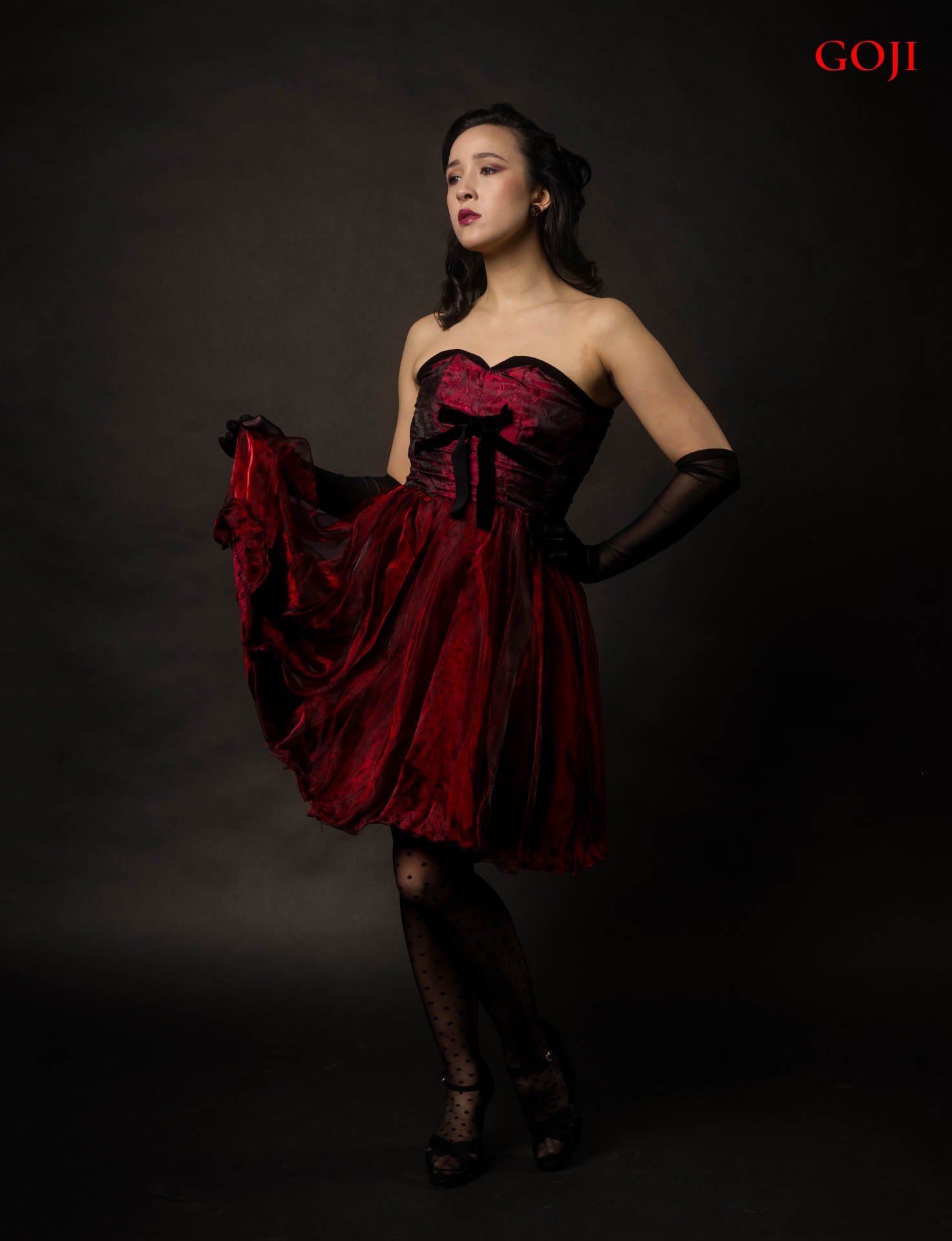 Crimson Poise editorial — GOJI Magazine — closing portrait of Victoria lifting the deep red skirt, contained composition, cinematic studio light, editorial fashion photography by Peter Scholz, Vienna