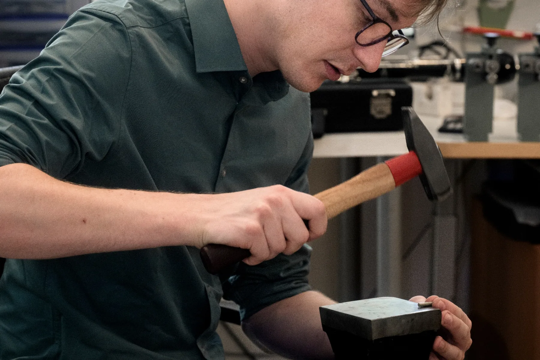 Florian Köck shaping a small metal component with a hammer on the anvil — precise, focused handwork at the bench.