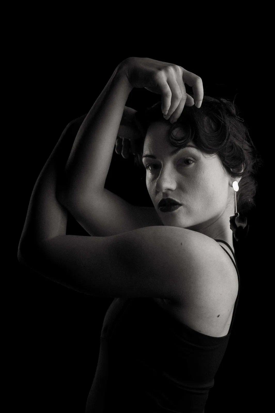 Sculptural black and white studio portrait — raised arms framing the face, the artistic climax of the Monochrome Presence editorial series